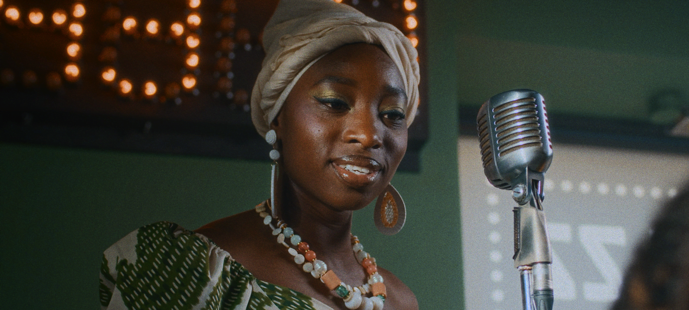 Film Grain — Woman in a headwrap performing beside a vintage microphone on a softly lit stage, with film grain effect.