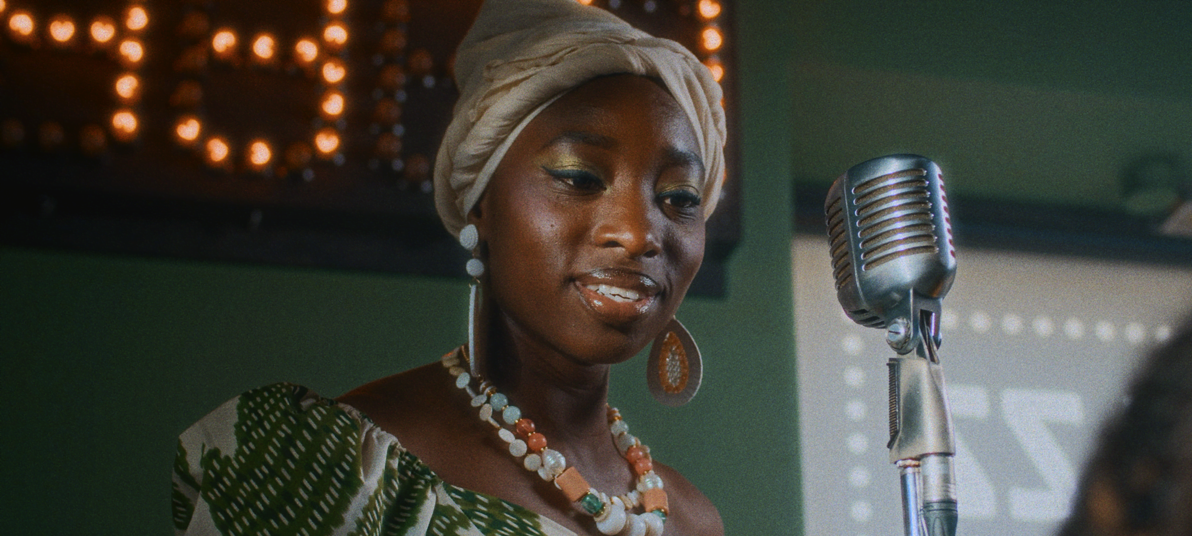 Bloom + Film Grain — Woman in a headwrap performing beside a vintage microphone on a softly lit stage, with bloom and film grain effects.