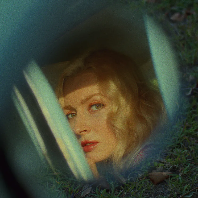 Fujichrome Velvia 100 — Blonde woman seen through a car window, framed by grass and soft reflections.