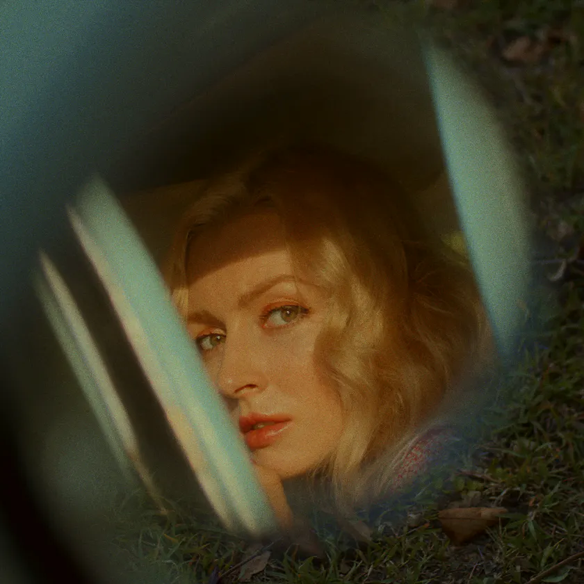 Cinestill 50D — Blonde woman seen through a car window, framed by grass and soft reflections.