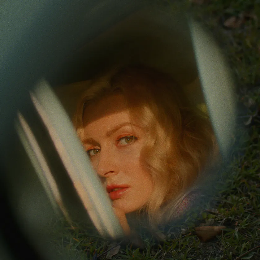 Kodak Ektar 25 Exp. 1996 — Blonde woman seen through a car window, framed by grass and soft reflections.