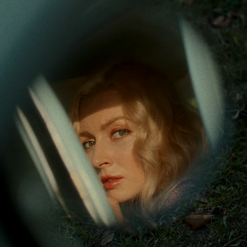 Kodak Aerocolor IV 126 — Blonde woman seen through a car window, framed by grass and soft reflections.