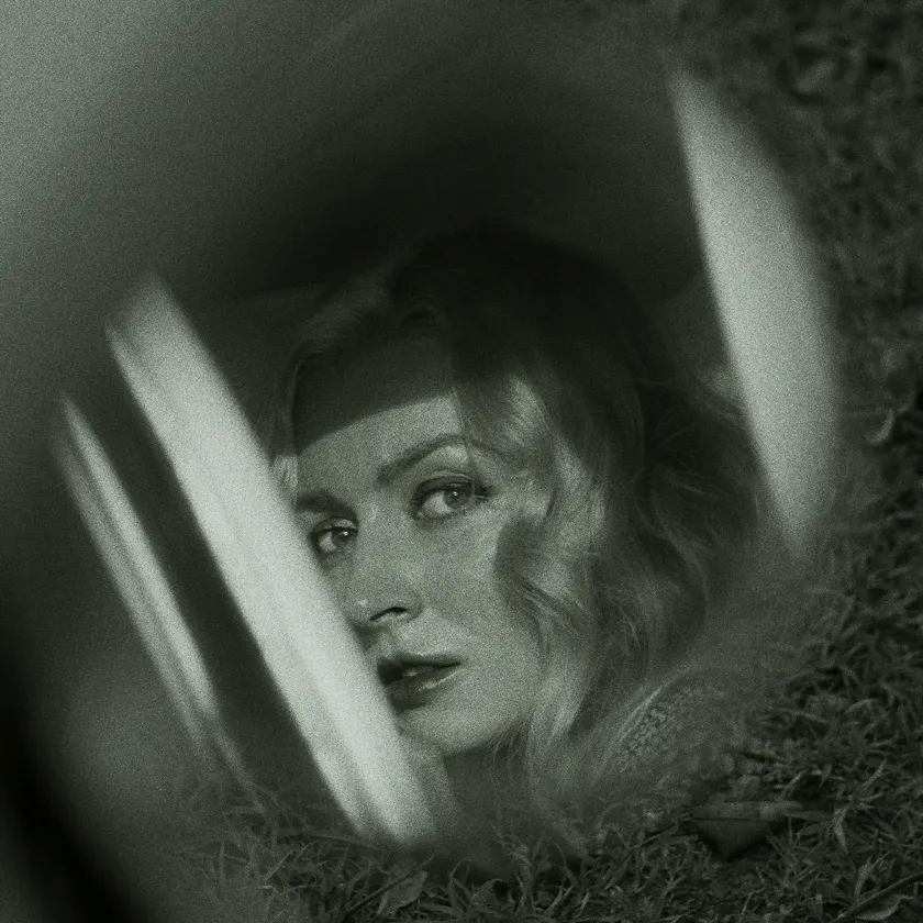 Rollei Ortho 26 — Black-and-white portrait of a blonde woman seen through a car window and grass.
