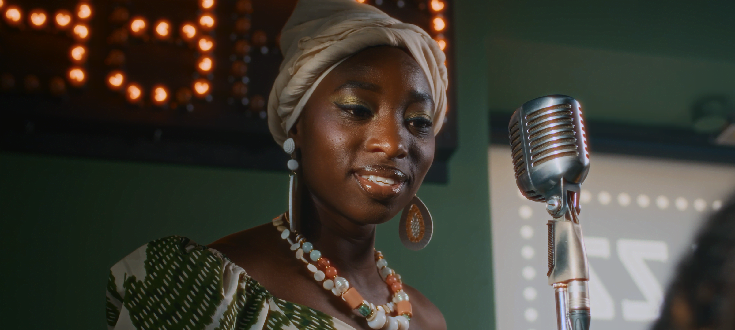 Halation — Woman in a headwrap performing beside a vintage microphone on a softly lit stage, with halation effect.